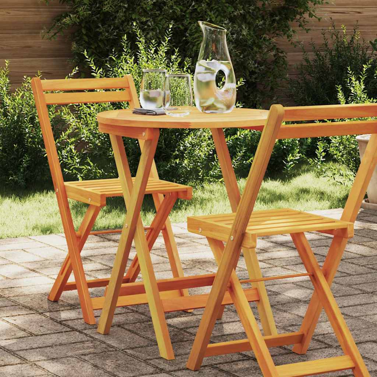 Holztisch und Stühle. Ein Glaskrug und zwei Gläser auf dem Tisch. Der Hintergrund umfasst Grün und eine Backstein-Terrasse.