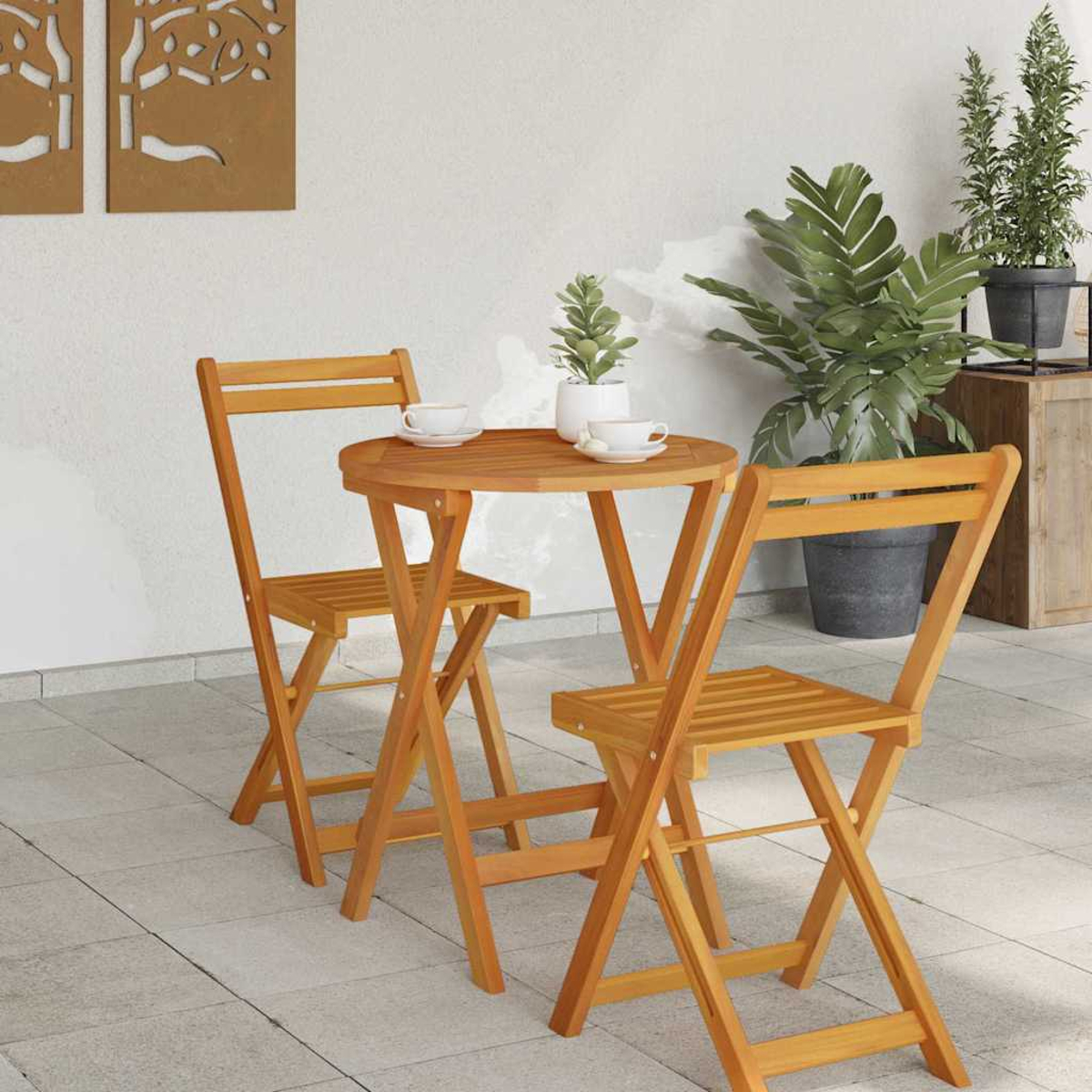 Holztisch und Stühle auf einer Terrasse. Zwei Stühle stehen dem Tisch mit Tassen gegenüber. Topfpflanzen befinden sich im Hintergrund.