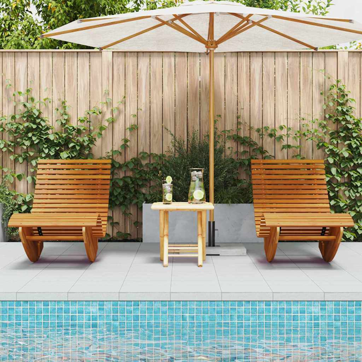 Zwei Holzliegen mit Sonnenschirm, Tisch mit Getränken und Pool im Vordergrund. Holzzaun und Pflanzen im Hintergrund.