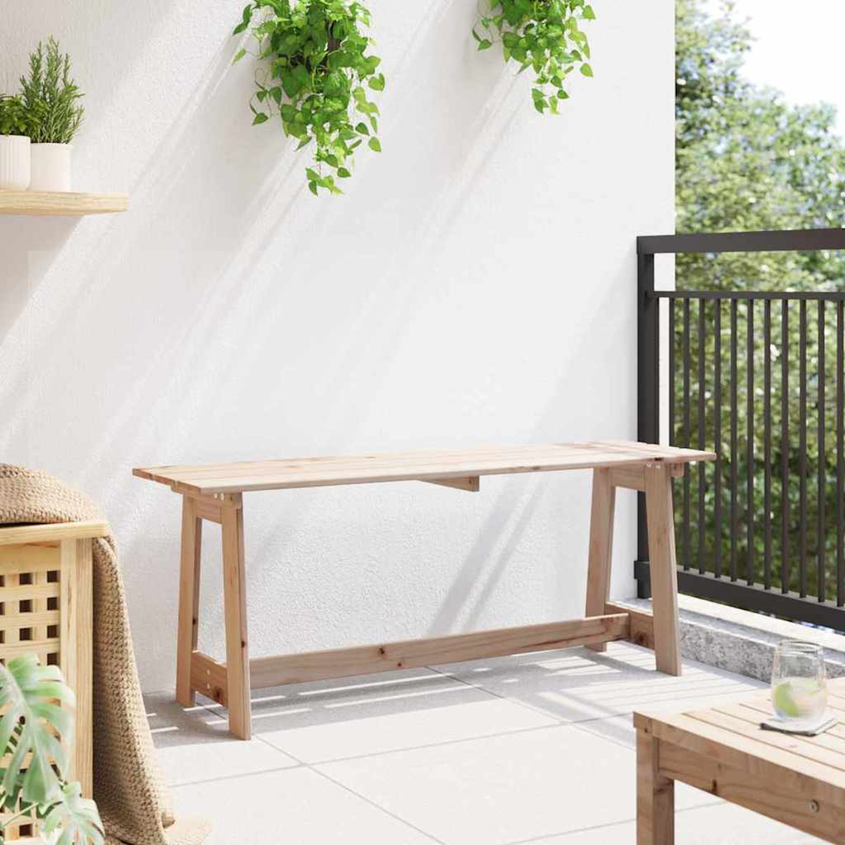 Holztisch auf einer Terrasse mit Pflanzen und einem Geländer. Pflanzen hängen von der Wand. Ein weiterer Tisch und Glas im Hintergrund.