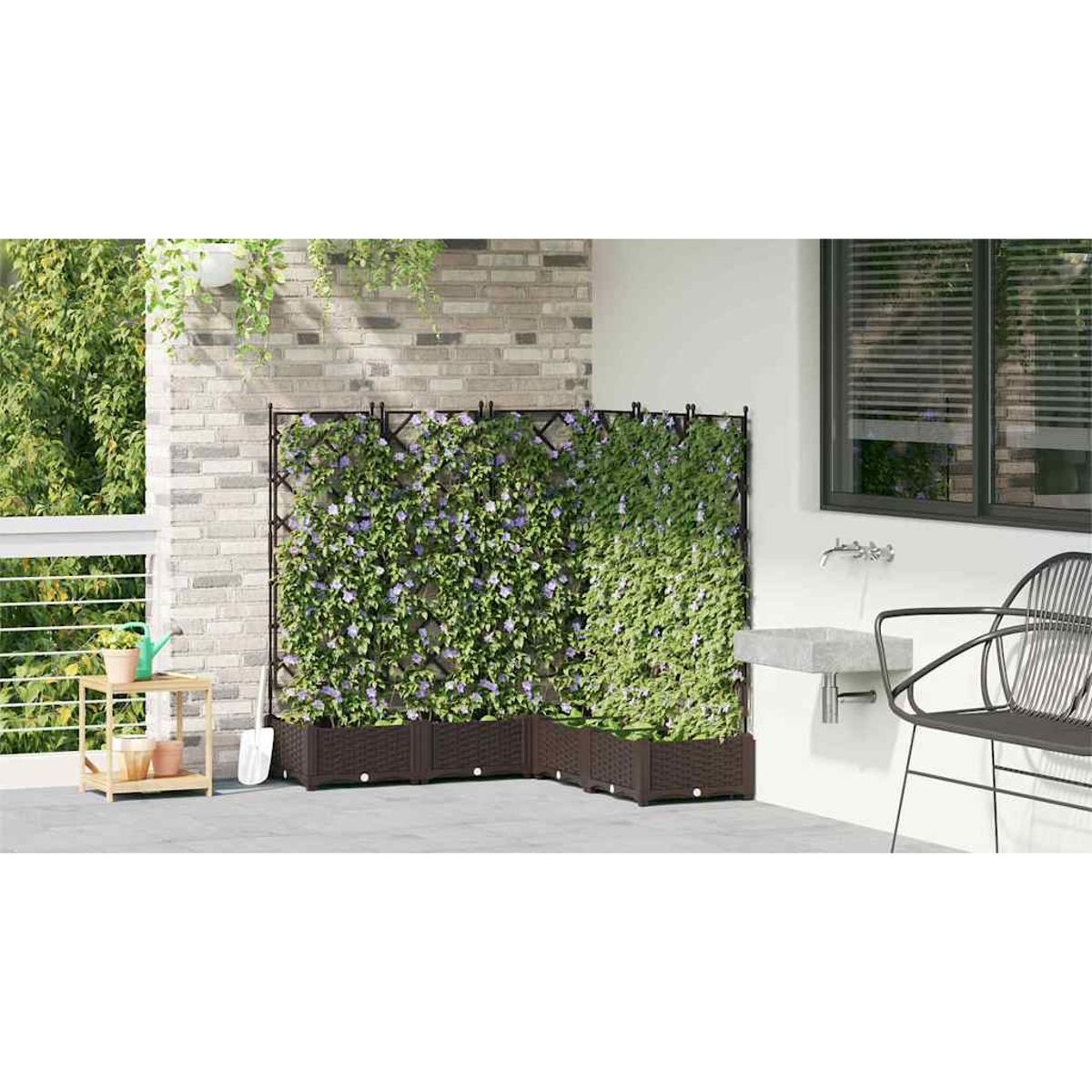 Eine Terrasse mit einer grünen Pflanzenwand mit lila Blumen. Braune Pflanzkästen stehen davor. Eine Backsteinmauer und ein Fenster sind im Hintergrund.
