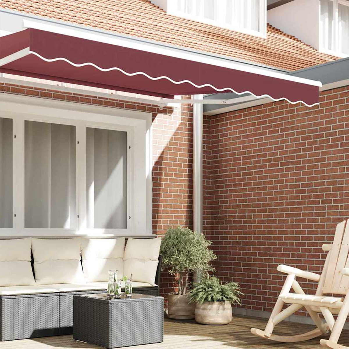 Eine Terrasse mit weinroter Markise. Ein Sofa mit Kissen, ein Tisch mit Getränken, Pflanzen und ein Schaukelstuhl sind sichtbar.