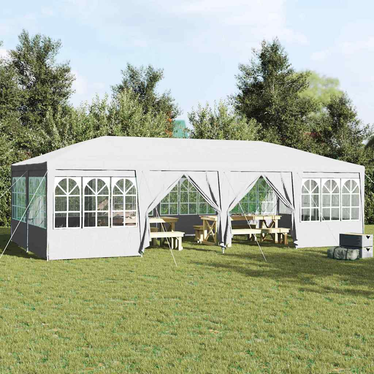 Una carpa blanca con ventanas y mesas de picnic está sobre hierba verde. Los árboles están en el fondo. Las cortinas grises están parcialmente abiertas.