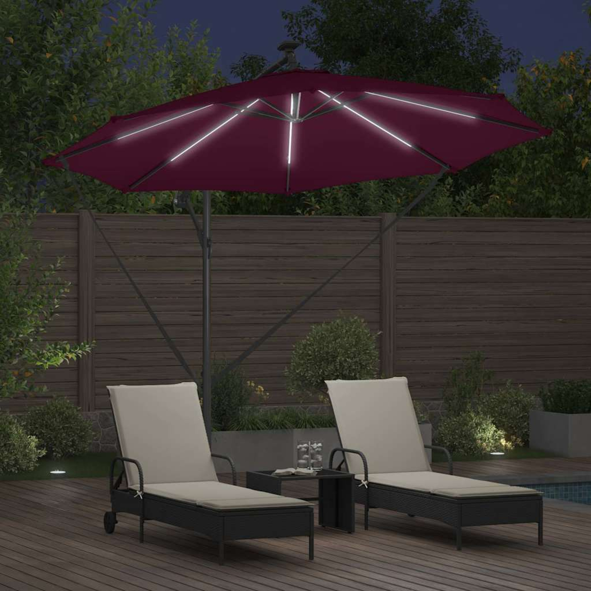 Una scena all'aperto di notte con un ombrello illuminato color bordeaux, due sedie a sdraio, un tavolino e una recinzione in legno sullo sfondo.