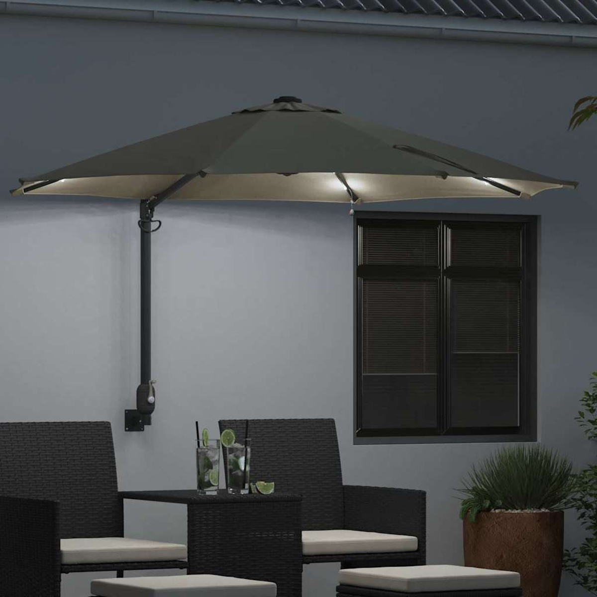 Patio esterno con un grande ombrellone illuminato, mobili neri e bevande su un tavolo. Una finestra sullo sfondo.