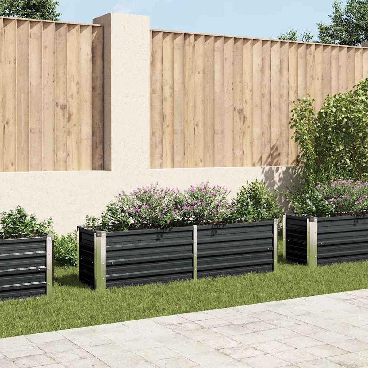 Drei dunkelgraue Pflanzgefäße mit Blumen stehen auf Gras. Ein Holzzaun und eine weiße Wand bilden den Hintergrund.