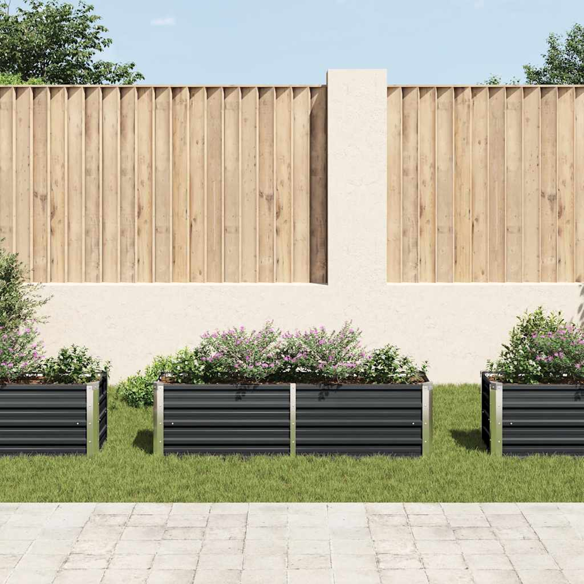 Drei schwarze Metallpflanzkästen mit Blumen auf grünem Gras, ein Holzzaun im Hintergrund und ein Steinweg im Vordergrund.