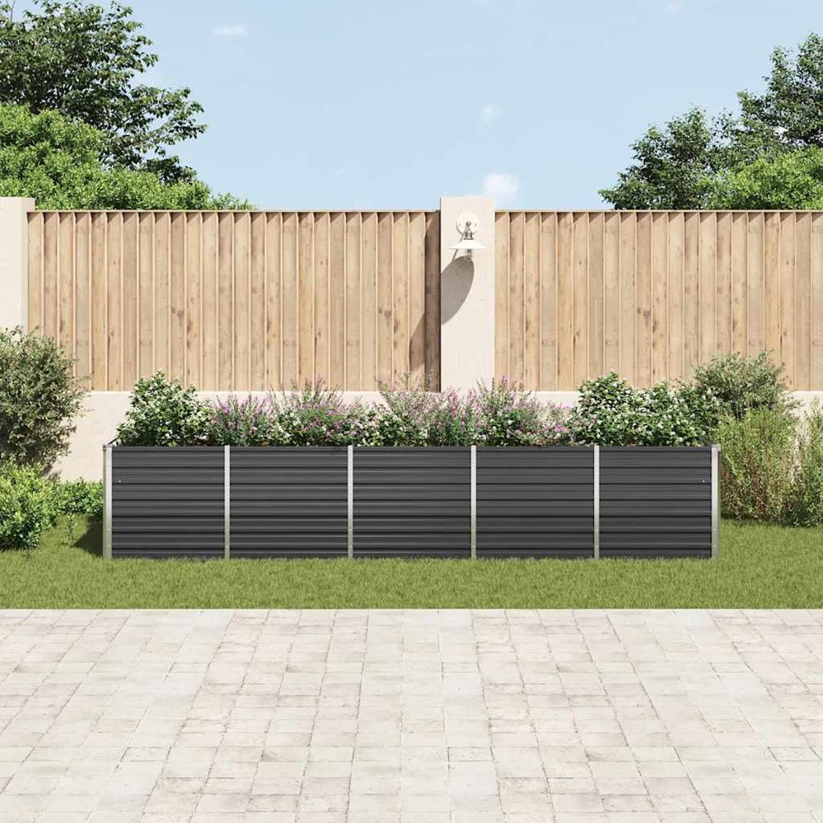 Eine Gartenszene mit grauem Metallzaun, Holzzaun und Pflanzen. Im Vordergrund eine gepflasterte Terrasse, im Hintergrund Bäume und Himmel.