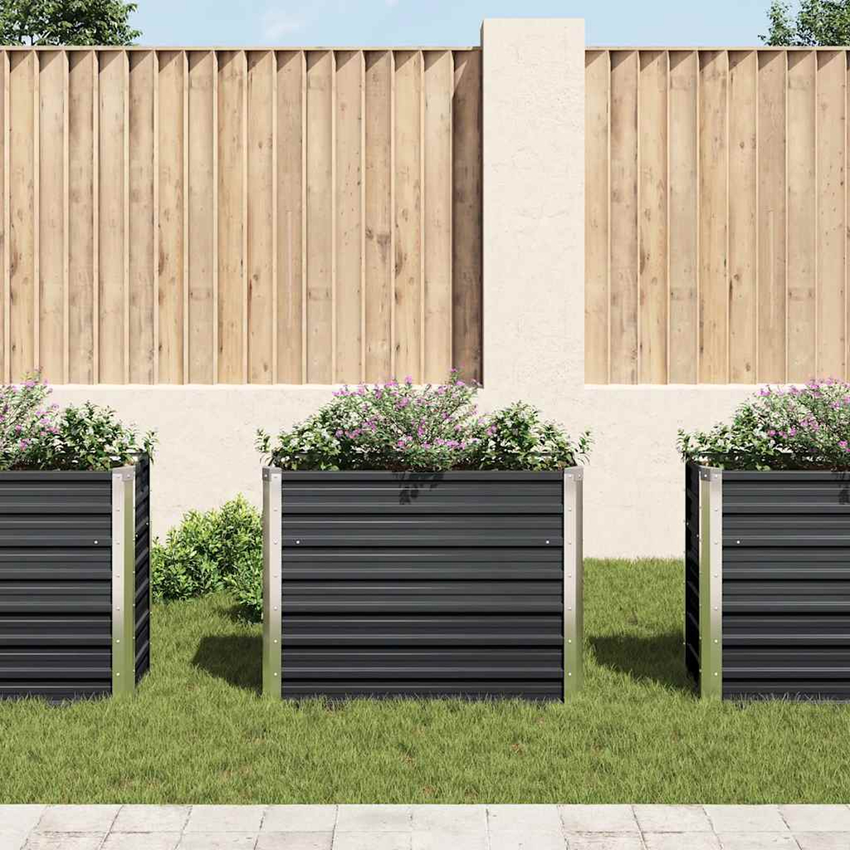 Drei schwarze Metallpflanzkästen mit Blumen stehen vor einem Holzzaun. Grünes Gras und ein Betonweg sind im Vordergrund.