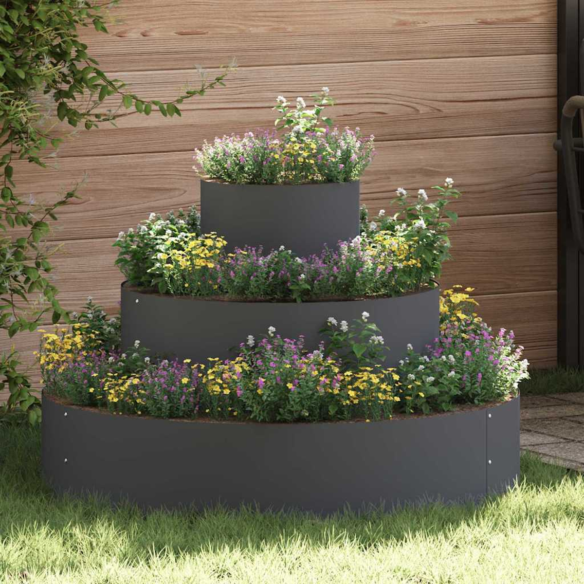 Ein gestuftes Gartenbeet mit bunten Blumen. Es steht im Gras, mit einem Holzzaun im Hintergrund und Kletterpflanzen an der Seite.
