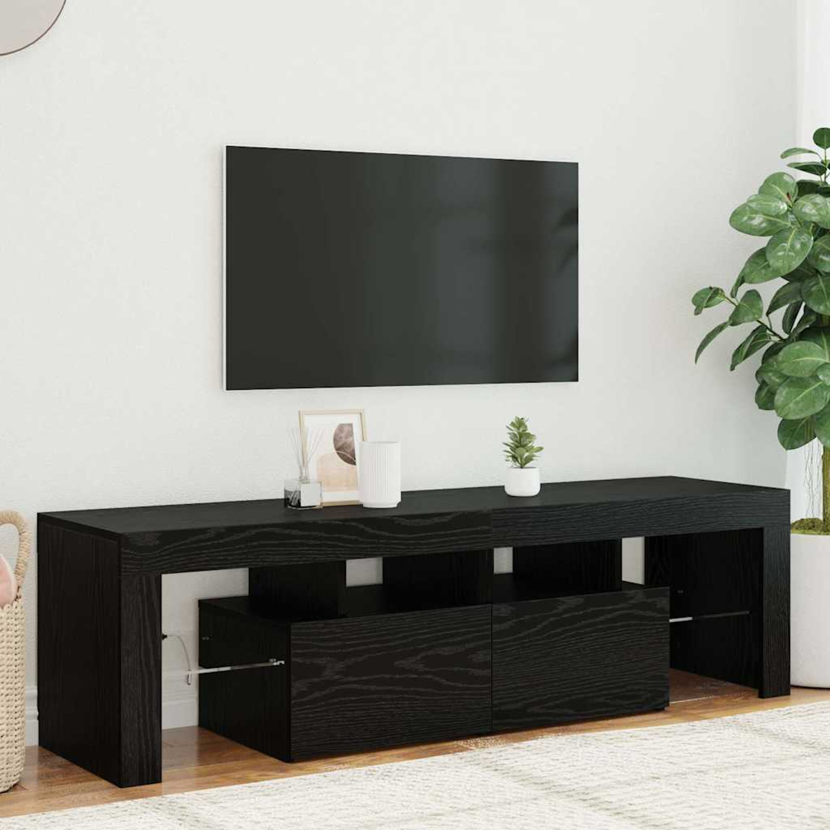 Ein schwarzer TV-Ständer mit einem Fernseher an einer weißen Wand. Eine kleine Pflanze und eine Vase stehen auf dem Ständer.