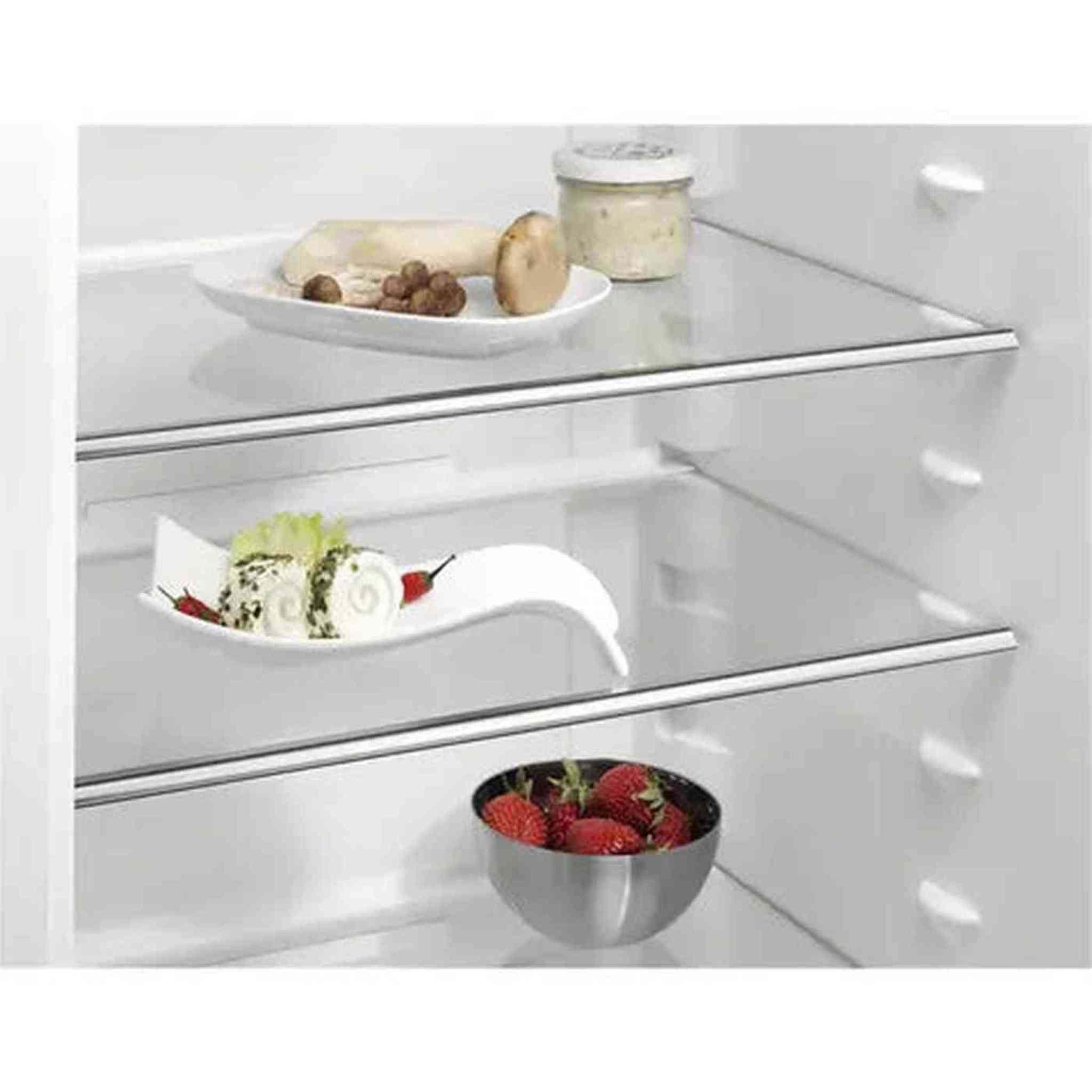 Interieur van de koelkast met planken. Bevat borden met eten, een kleine kom aardbeien en potjes. Goed verlicht.