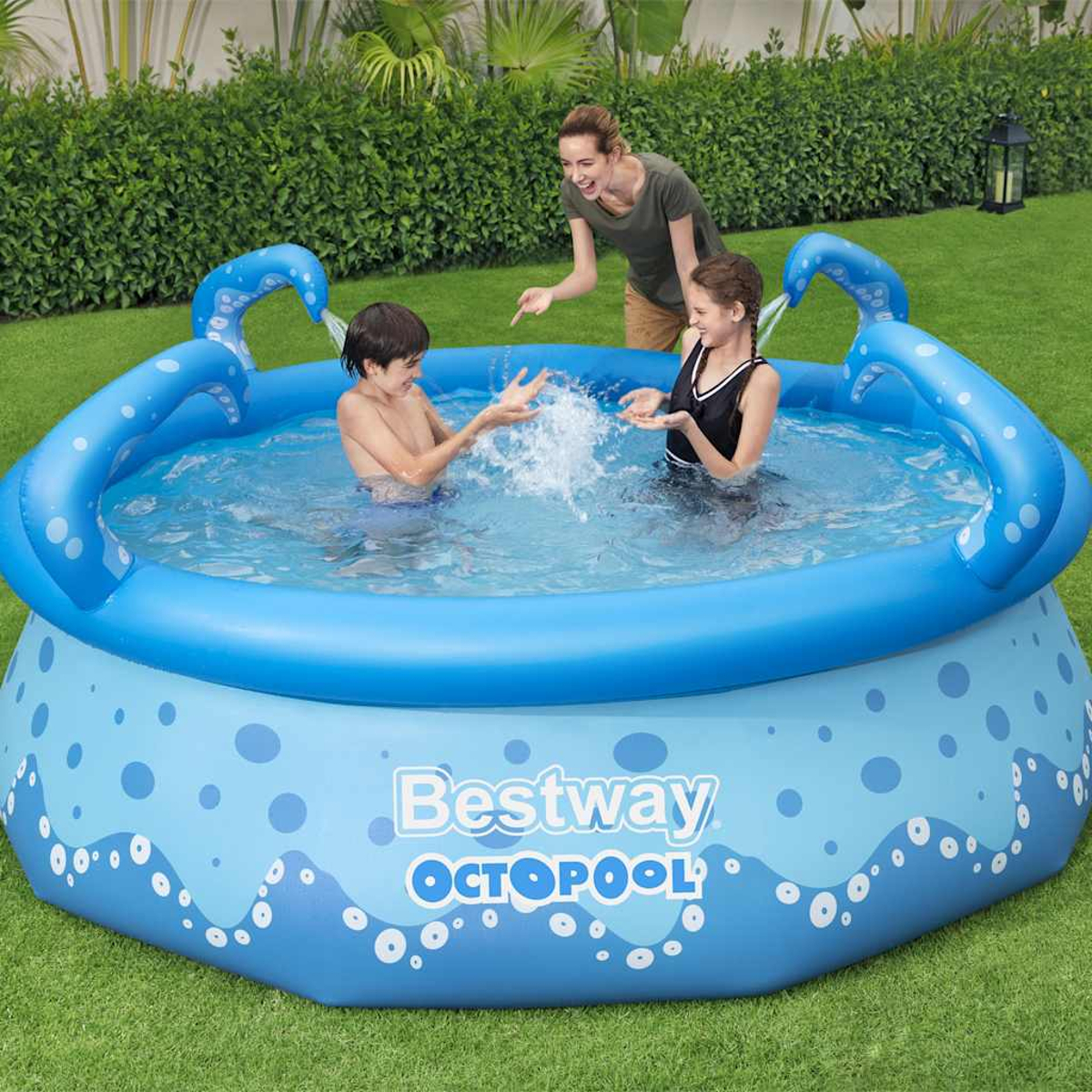 Drei Personen spielen in einem aufblasbaren blauen Pool. Eine Frau und zwei Kinder spritzen Wasser. Der Pool befindet sich auf einer grünen Wiese.