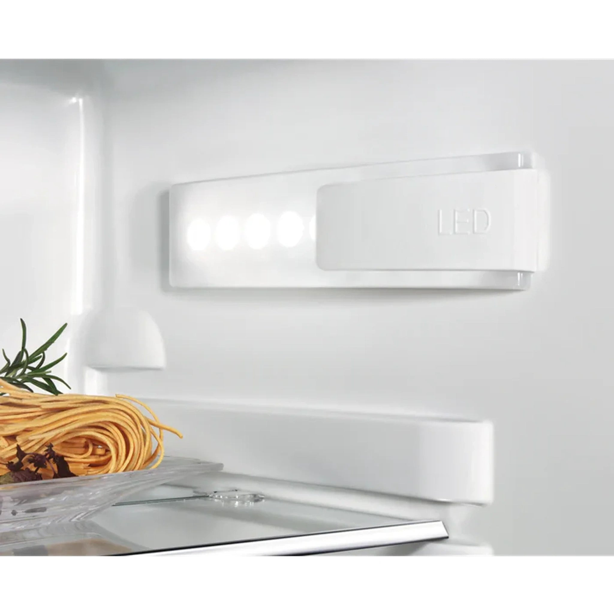 In een witte koelkast bevindt zich een led-armatuur en een plank met pasta en kruiden. Het interieur is wit.