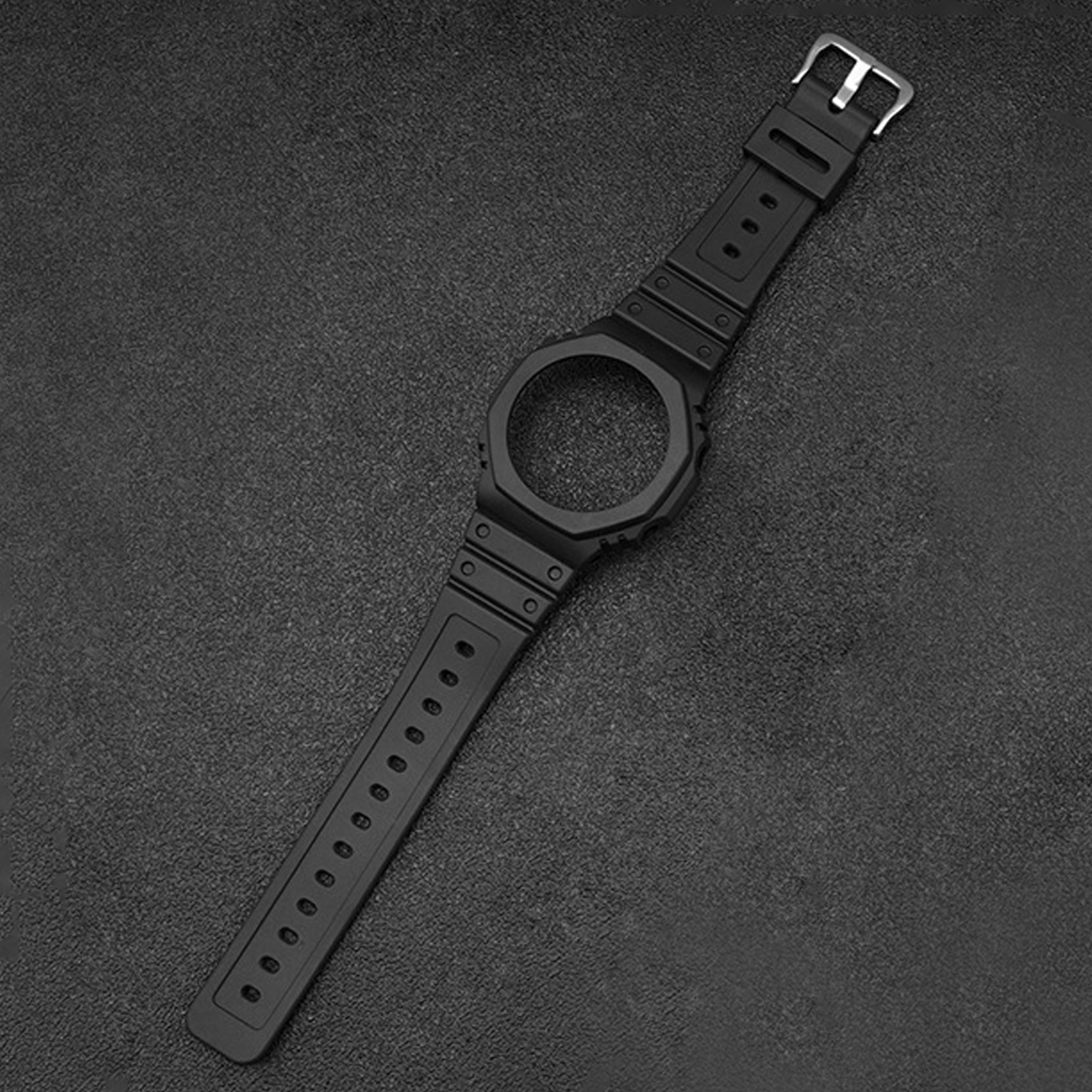 Ein schwarzes Uhrenarmband mit silberner Schnalle liegt auf einer strukturierten, dunkelgrauen Oberfläche. Das Zifferblatt fehlt.