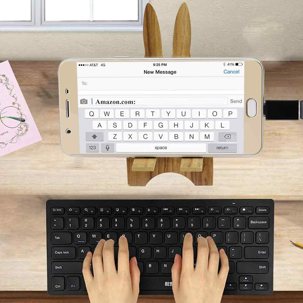 Ein Telefon auf einem Holzständer zeigt einen neuen Nachrichtenbildschirm. Unten befindet sich eine schwarze Tastatur, und Hände tippen.