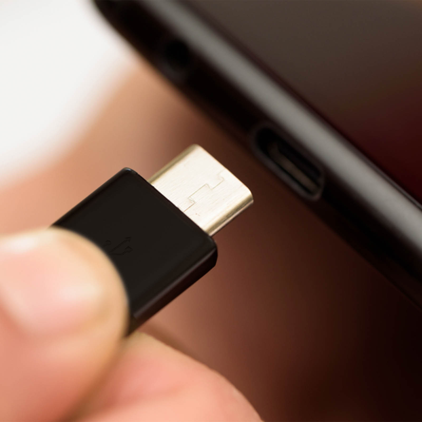 Una mano inserisce un connettore USB-C nero in un telefono. Il connettore è argento e nero, il telefono è nero.
