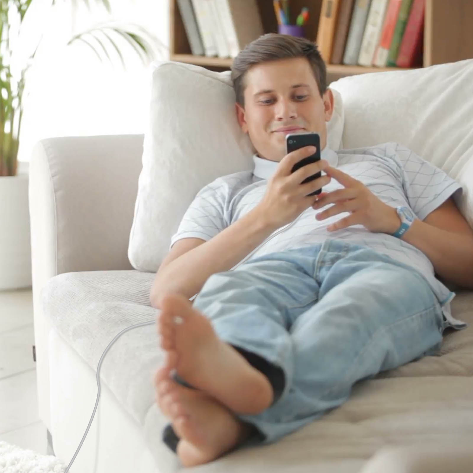 Un uomo si rilassa su un divano, guardando il telefono. Indossa jeans e una camicia azzurra.