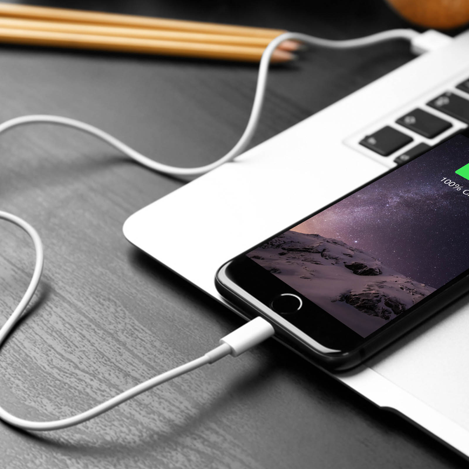 Smartphone noir en charge sur un ordinateur portable. Le téléphone affiche une scène de nuit étoilée. Câble blanc connecté.