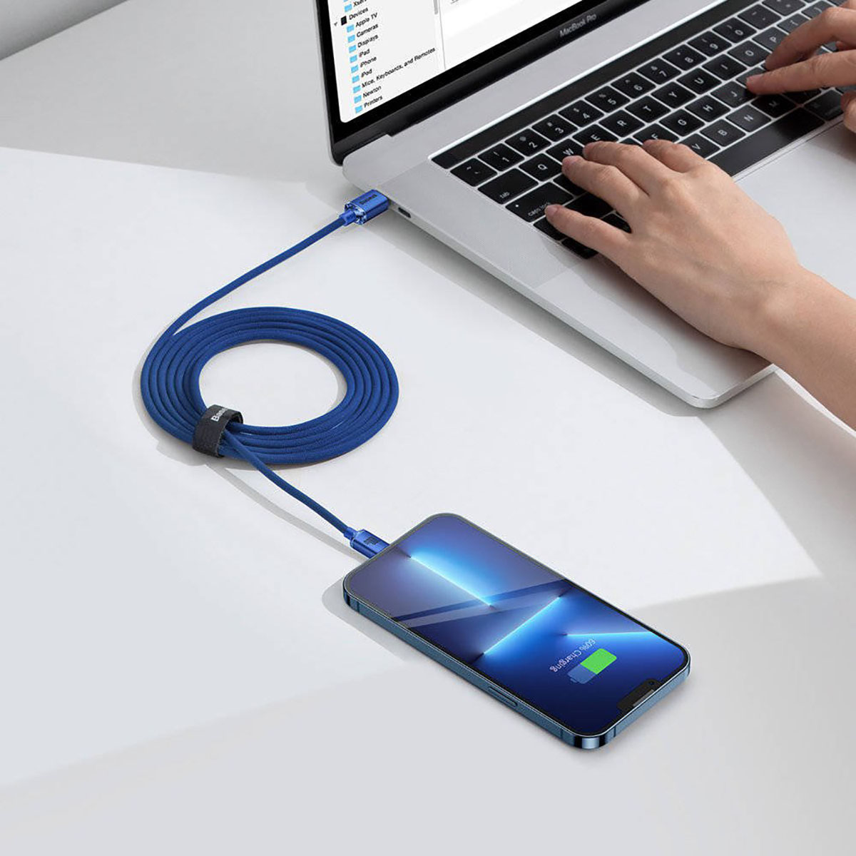Il cavo di ricarica blu collega un telefono a un laptop. Il telefono mostra il 60% di carica. Una mano digita sulla tastiera.