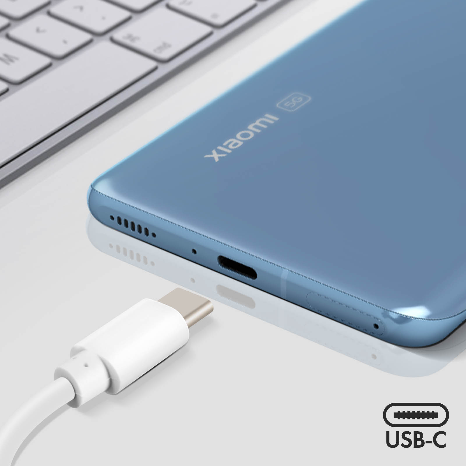 Telefono Xiaomi blu con cavo USB-C collegato. Una tastiera è sullo sfondo. Il telefono ha il logo 5G.