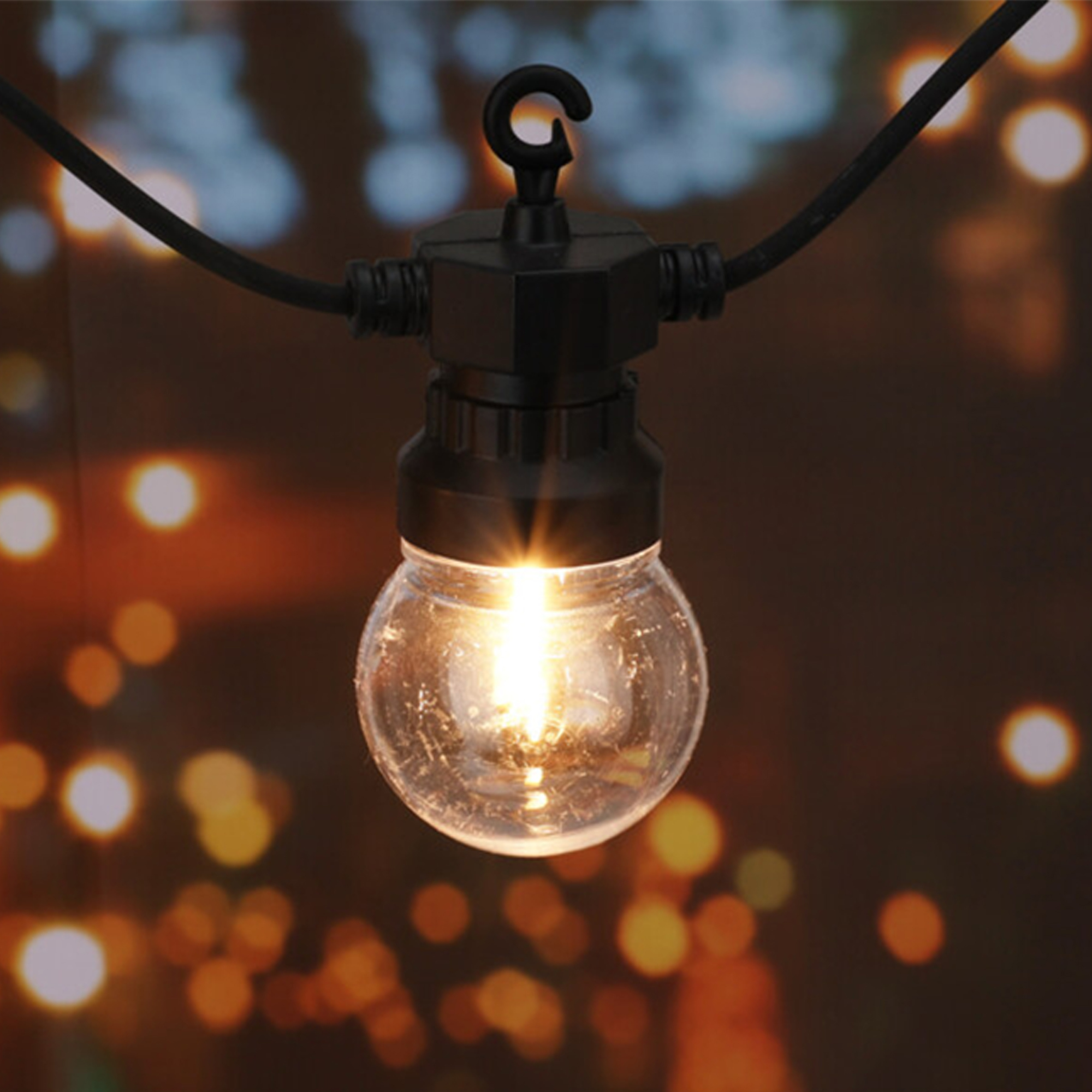 Primer plano de una bombilla redonda encendida que cuelga de un cable negro. El fondo está borroso con luces cálidas de bokeh.