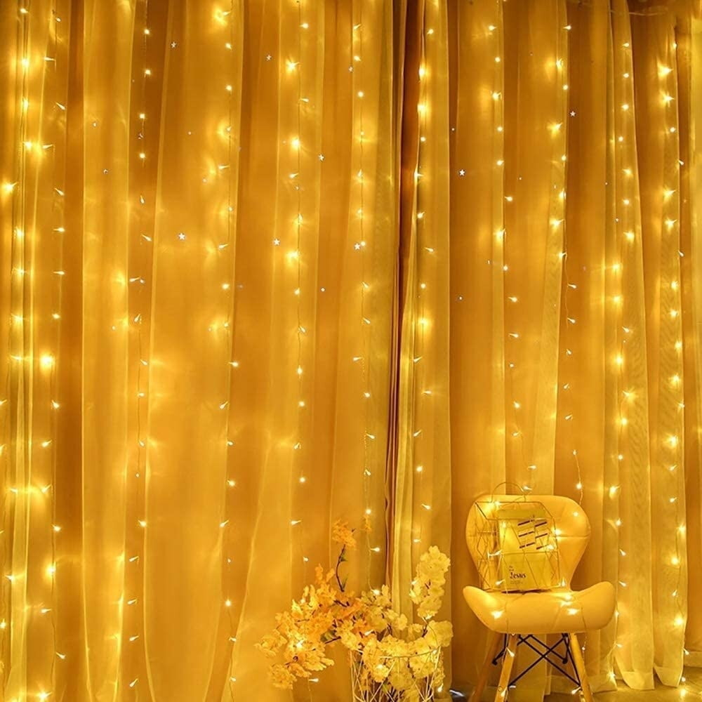 Gelbe Vorhänge mit Lichterketten. Ein Stuhl mit einer Box und Blumen. Die Lichter verleihen der Szene einen warmen, einladenden Glanz.