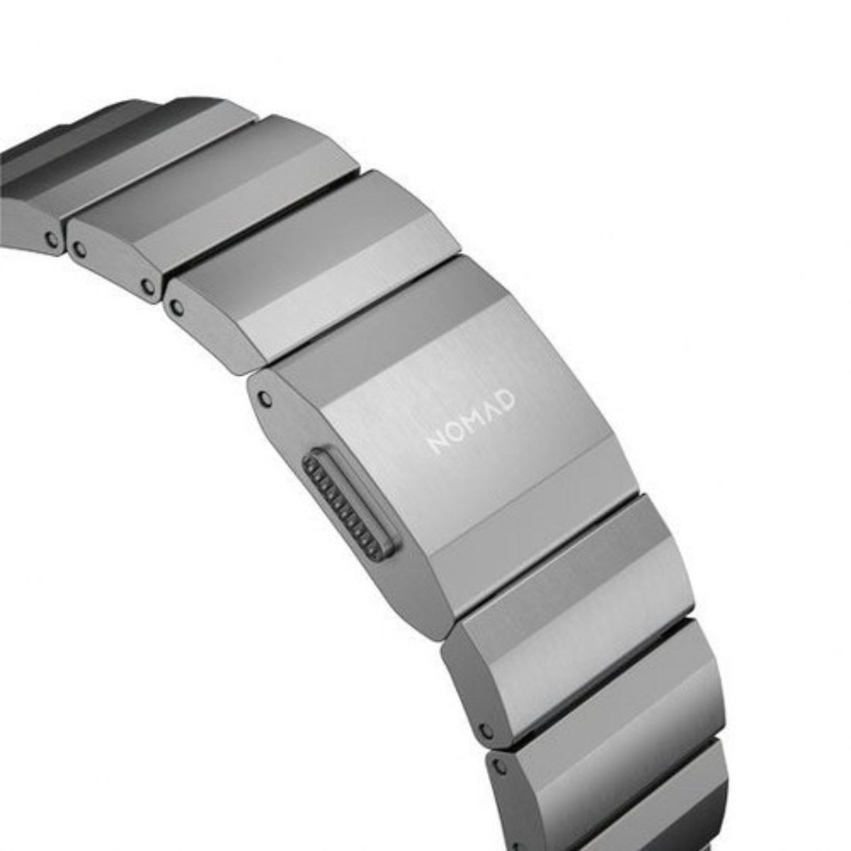 Primer plano de una correa de reloj plateada. Visible la marca 'NOMAD'. La correa es de eslabones metálicos conectados.