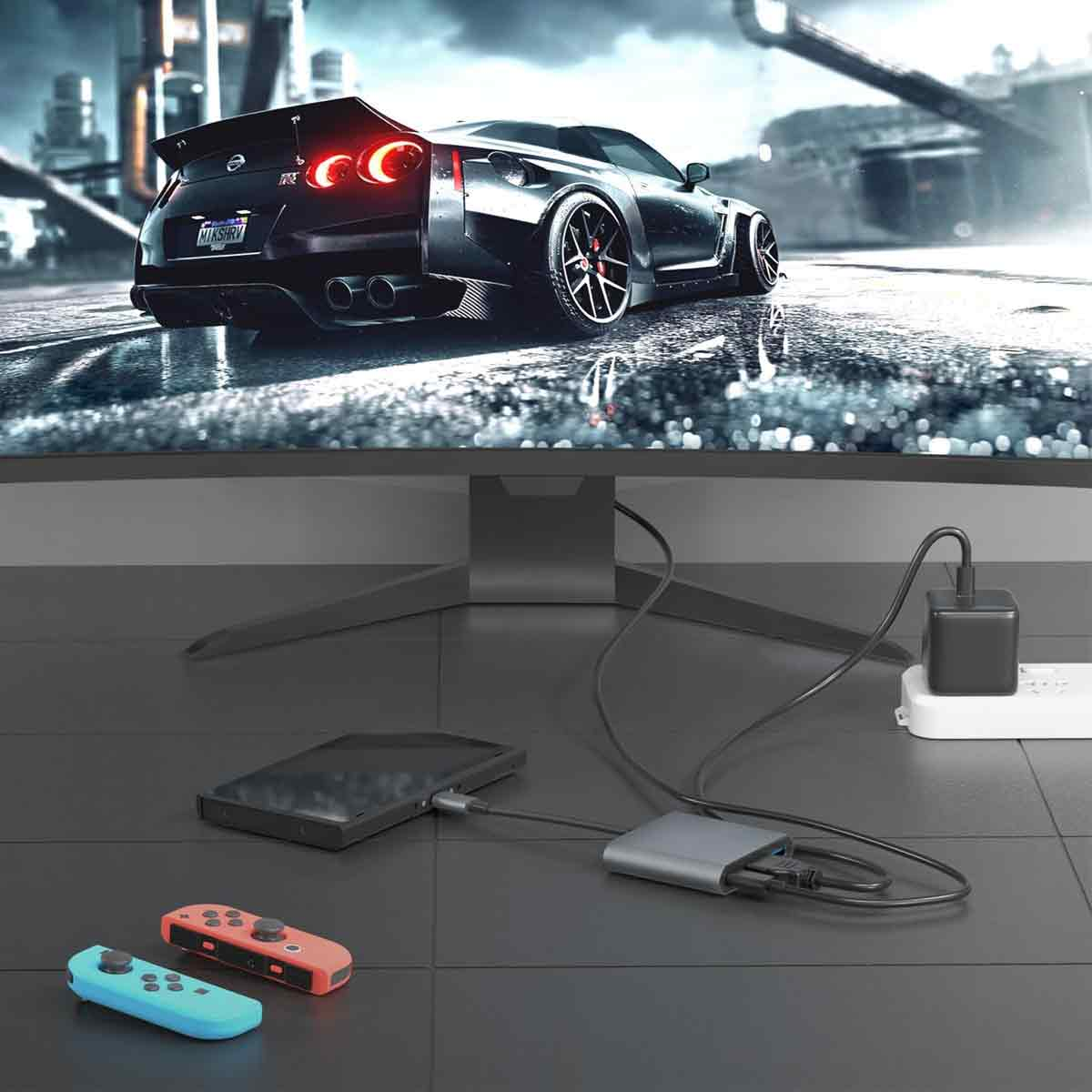 Schwarzes Auto auf dem Monitor. Darunter ein Telefon, ein Hub und Controller. Netzteil und Steckerleiste sind auch sichtbar.