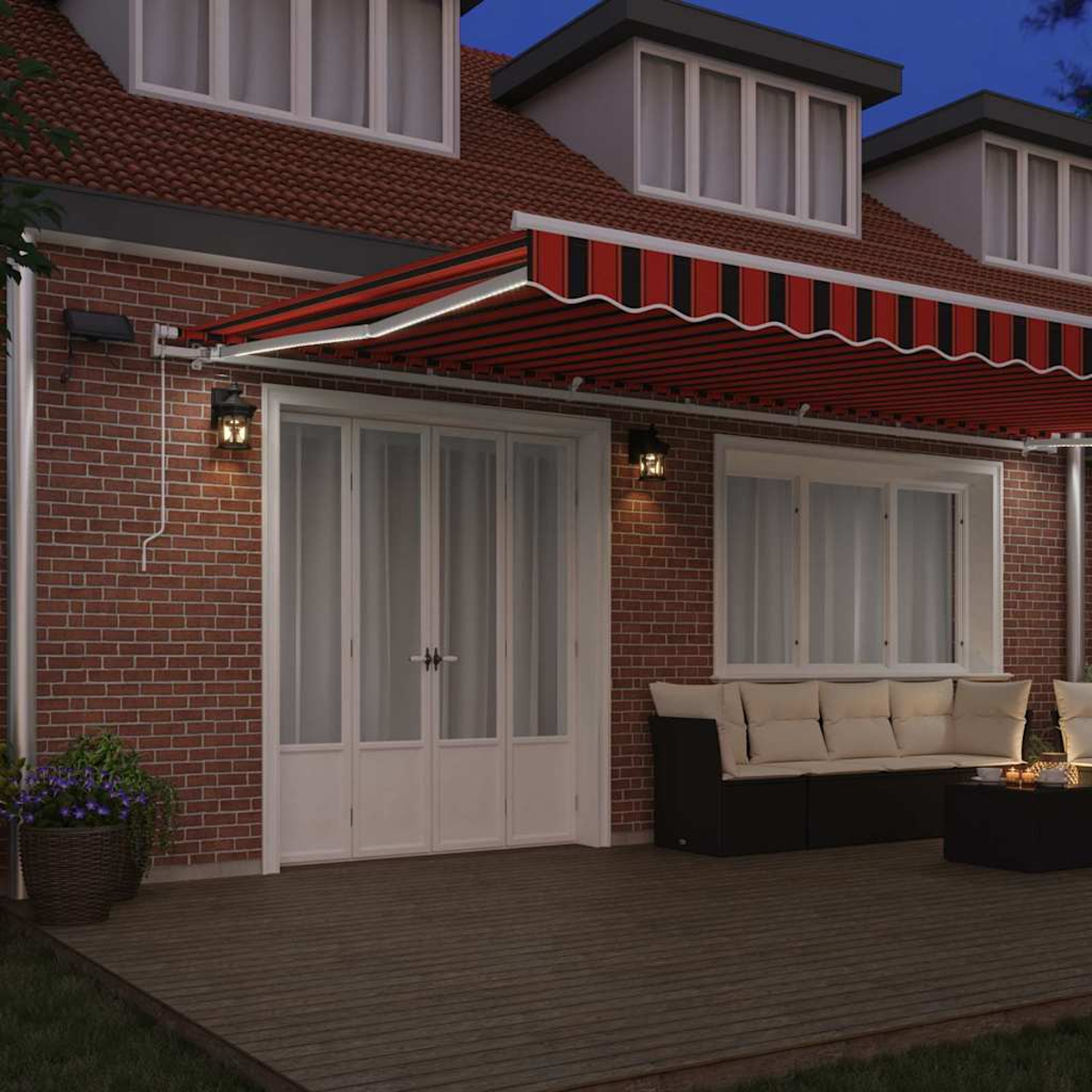 Ein Haus mit rot-schwarz gestreifter Markise. Eine Terrasse mit Sofa und Tisch. Backsteinfassade mit weißen Türen und Fenstern.