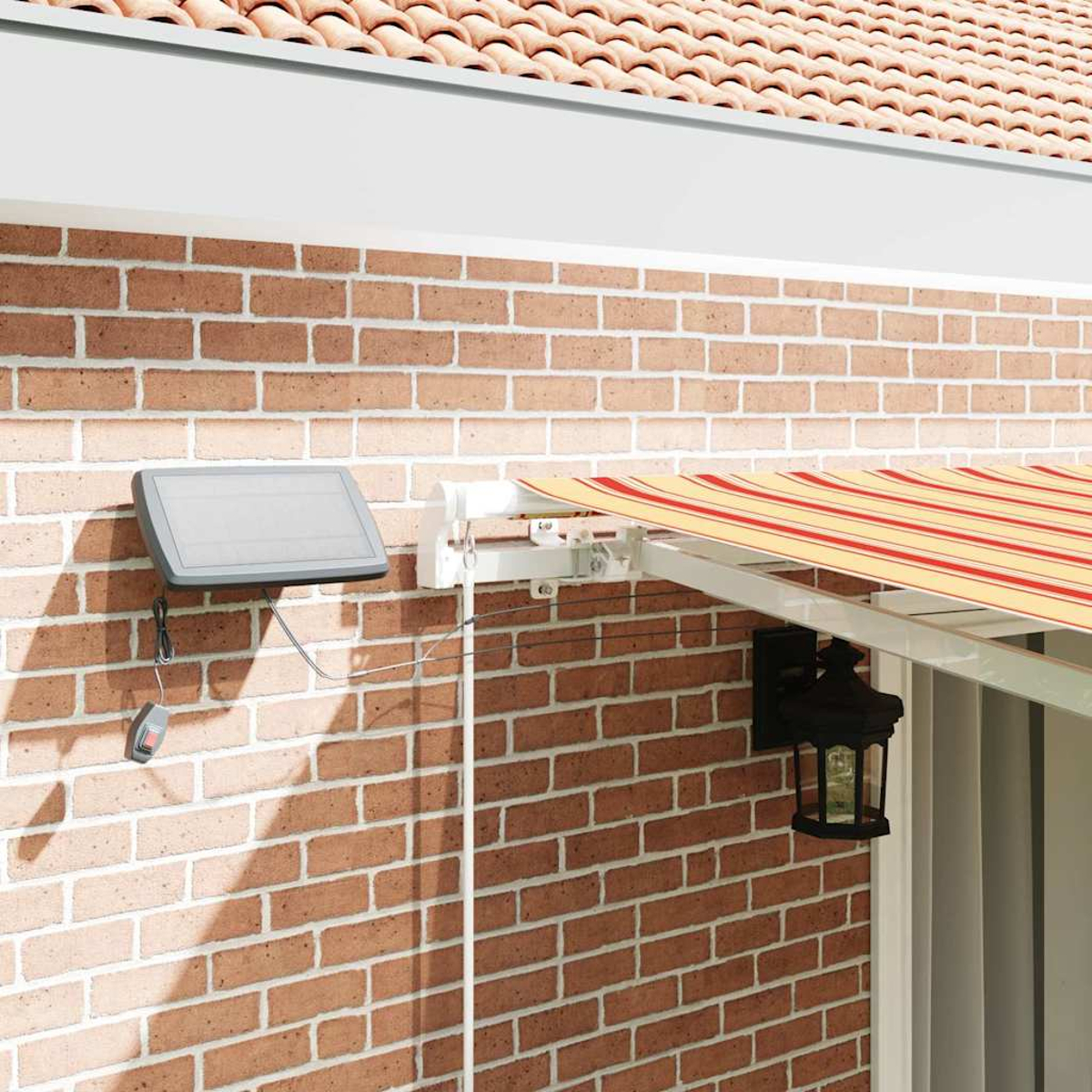 Eine Backsteinmauer mit Solarpanel, Markise und Lampe. Die Markise hat rot-gelbe Streifen. Dachziegel im Hintergrund.