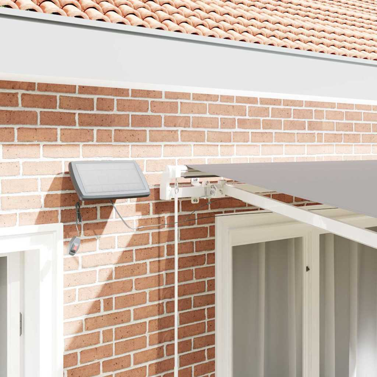 Eine Backsteinmauer mit einer grauen Markise. Auf der Wand ist ein Solarpanel montiert. Unter der Markise befinden sich zwei weiß umrahmte Fenster.