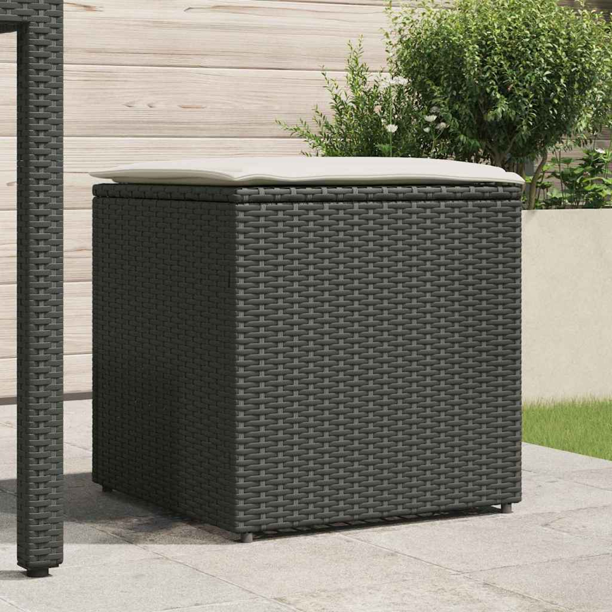 Eine dunkelgraue, gewebte Aufbewahrungsbox mit einem weißen Kissen oben. Sie steht auf einer Terrasse mit Holzzaun und Grün im Hintergrund.