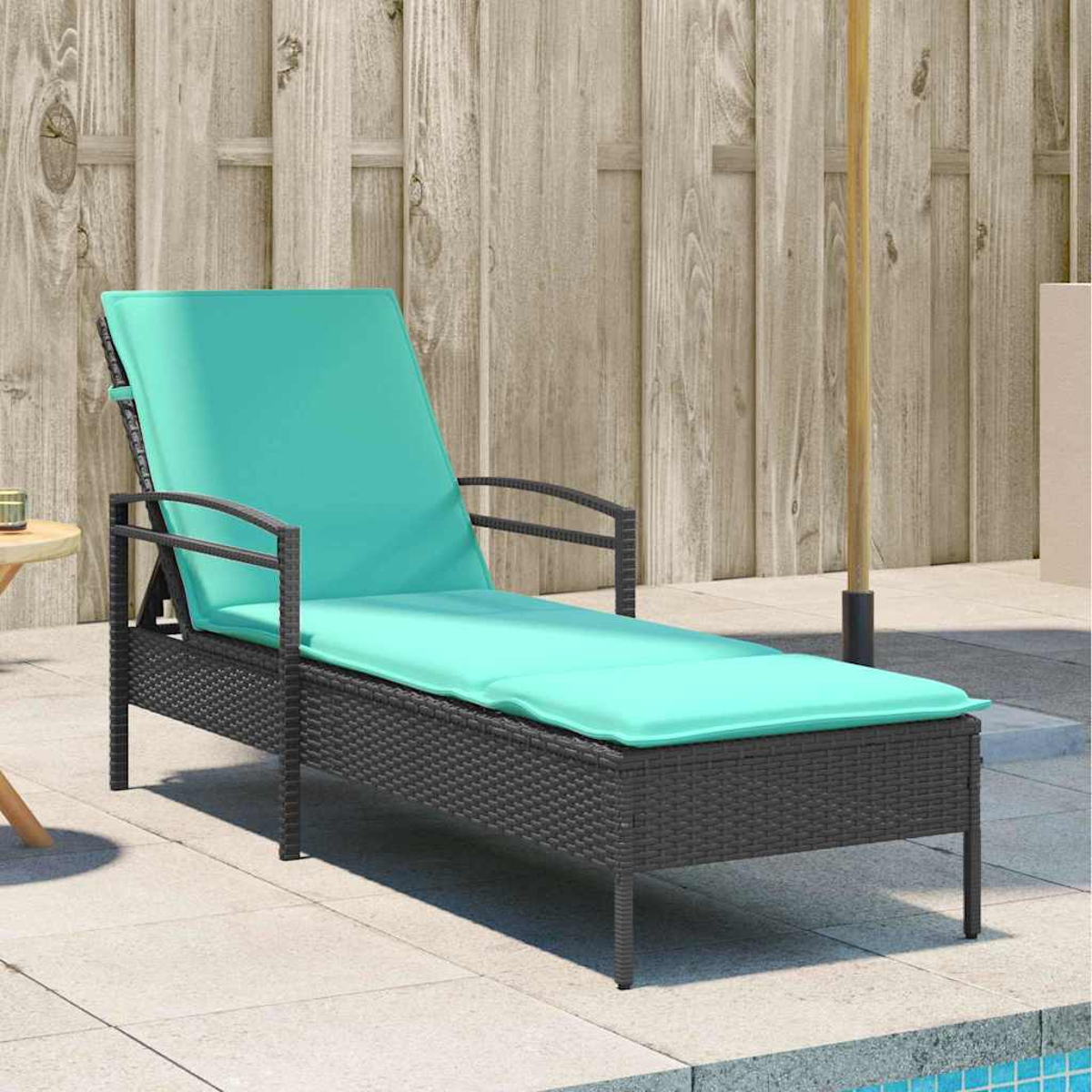 Eine dunkelgraue Wicker-Chaiselongue mit einem türkisfarbenen Kissen steht auf einer Terrasse. Im Hintergrund ist ein Holzzaun zu sehen.