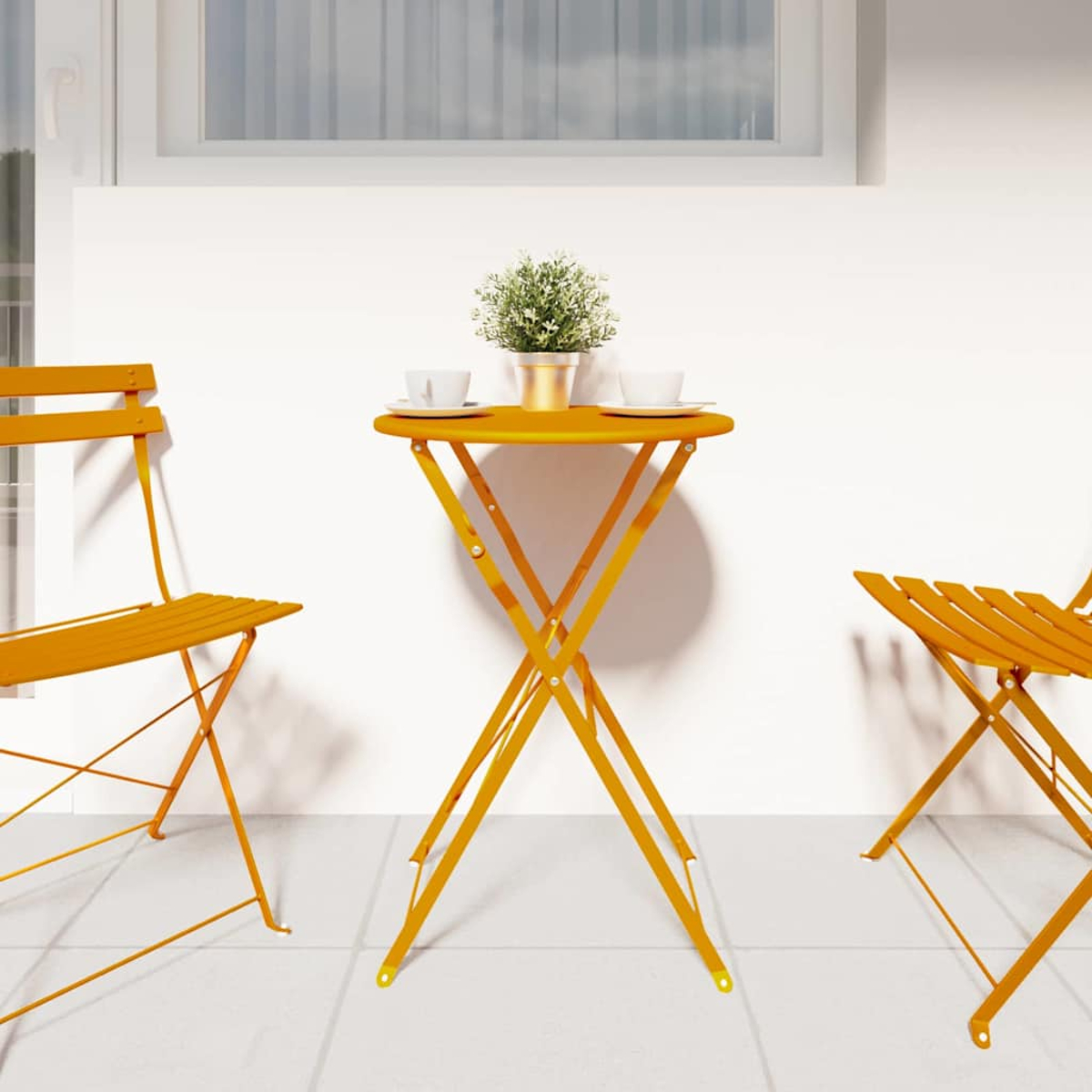 Ein gelber Tisch und Stühle stehen auf einer Terrasse. Auf dem Tisch stehen zwei Tassen und eine Pflanze. Im Hintergrund eine weiße Wand und ein Fenster.