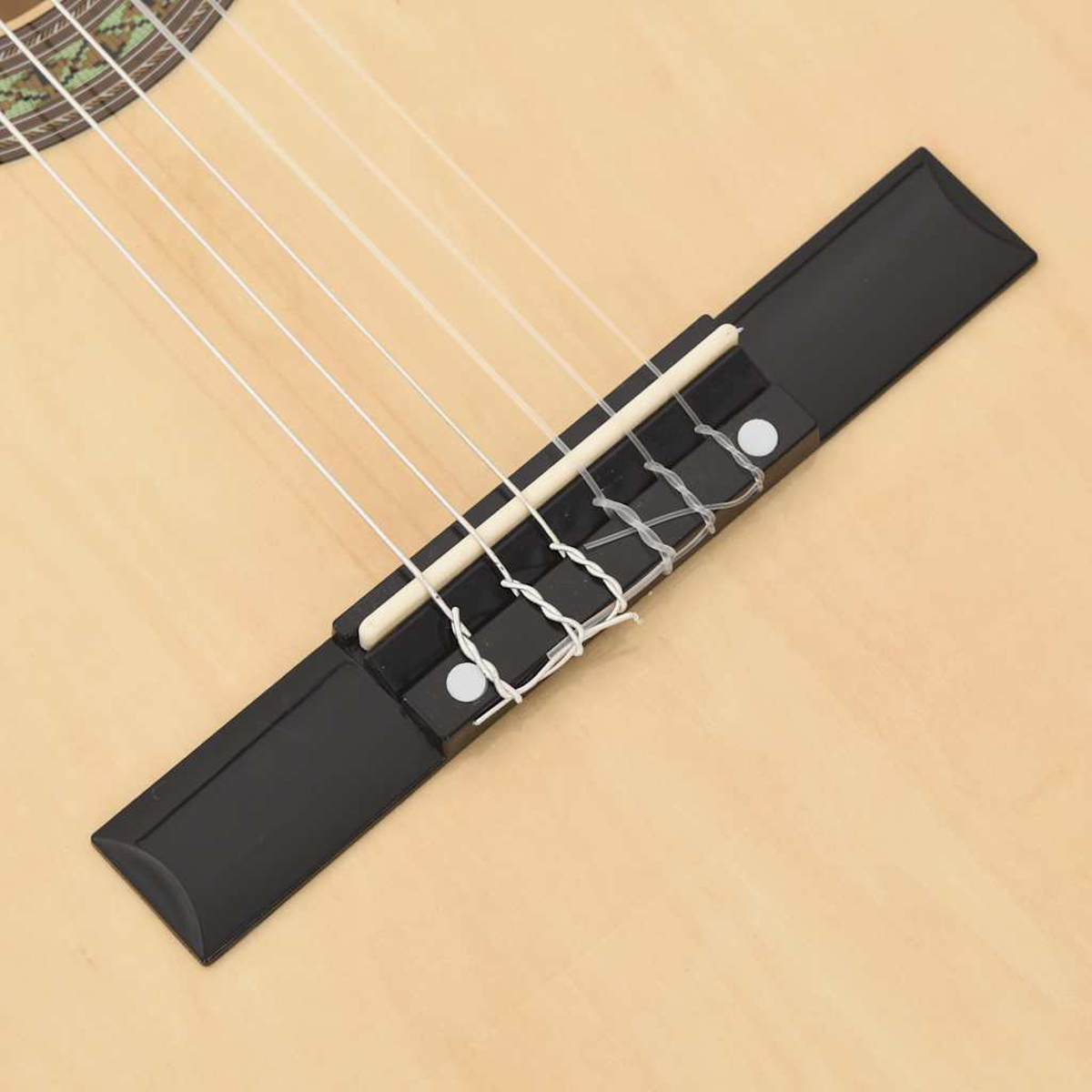 Nahaufnahme einer Gitarrenbrücke. Schwarze Brücke mit weißen Saiten und weißen Stiften auf hellem Holz.