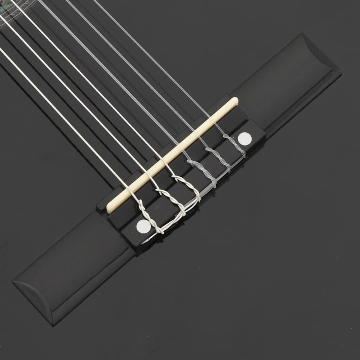 Nahaufnahme einer schwarzen Gitarrenbrücke mit Saiten. Weiße Saiten sind über eine schwarze Brücke mit einem hellen Holzstück gespannt.