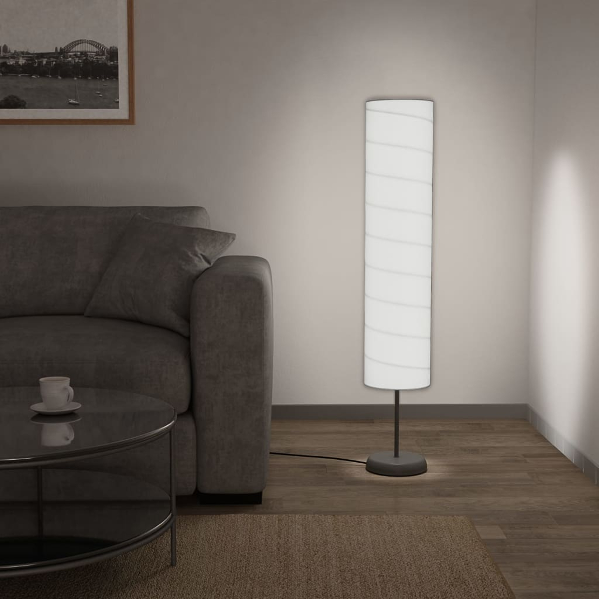 Ein Wohnzimmer mit grauem Sofa, Stehlampe, Couchtisch mit Tasse und gerahmtem Bild an der Wand.