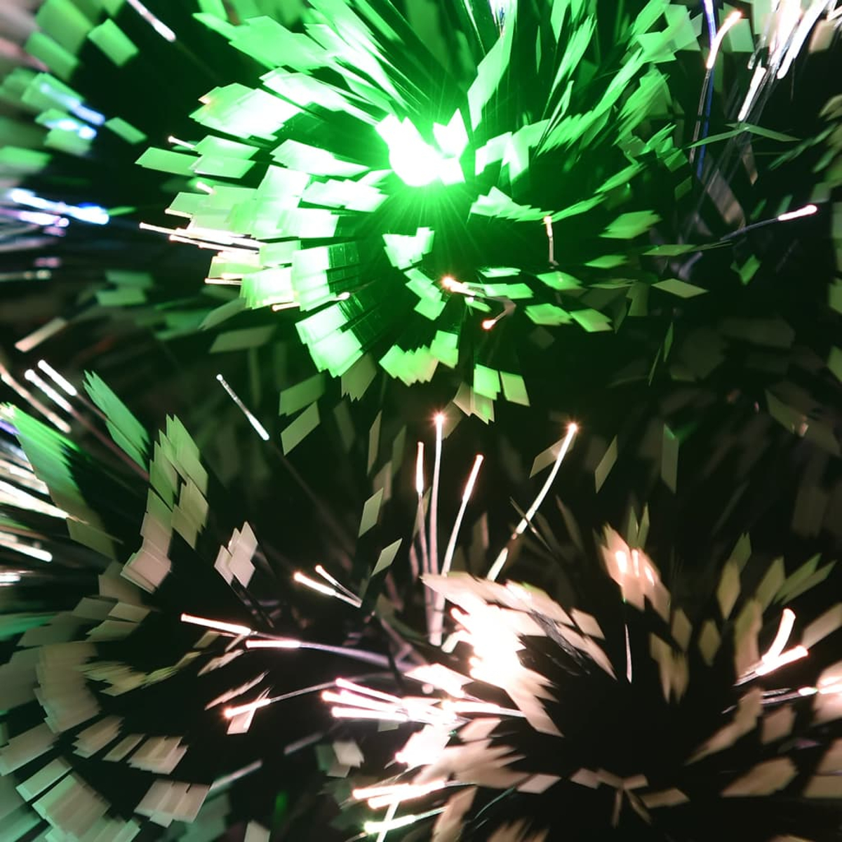 Nahaufnahme eines Weihnachtsbaums mit grünen und weißen Lichtern. Die Lichter erzeugen einen funkelnden Effekt, mit dunklem Hintergrund.
