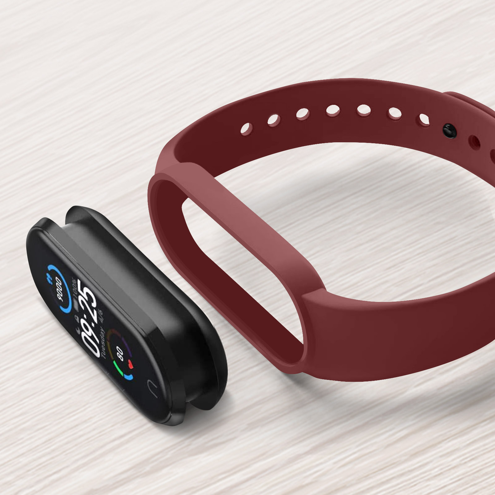 Un fitness tracker nero e un cinturino rosso staccato sono su una superficie di legno chiaro. Il tracker mostra ora e statistiche.
