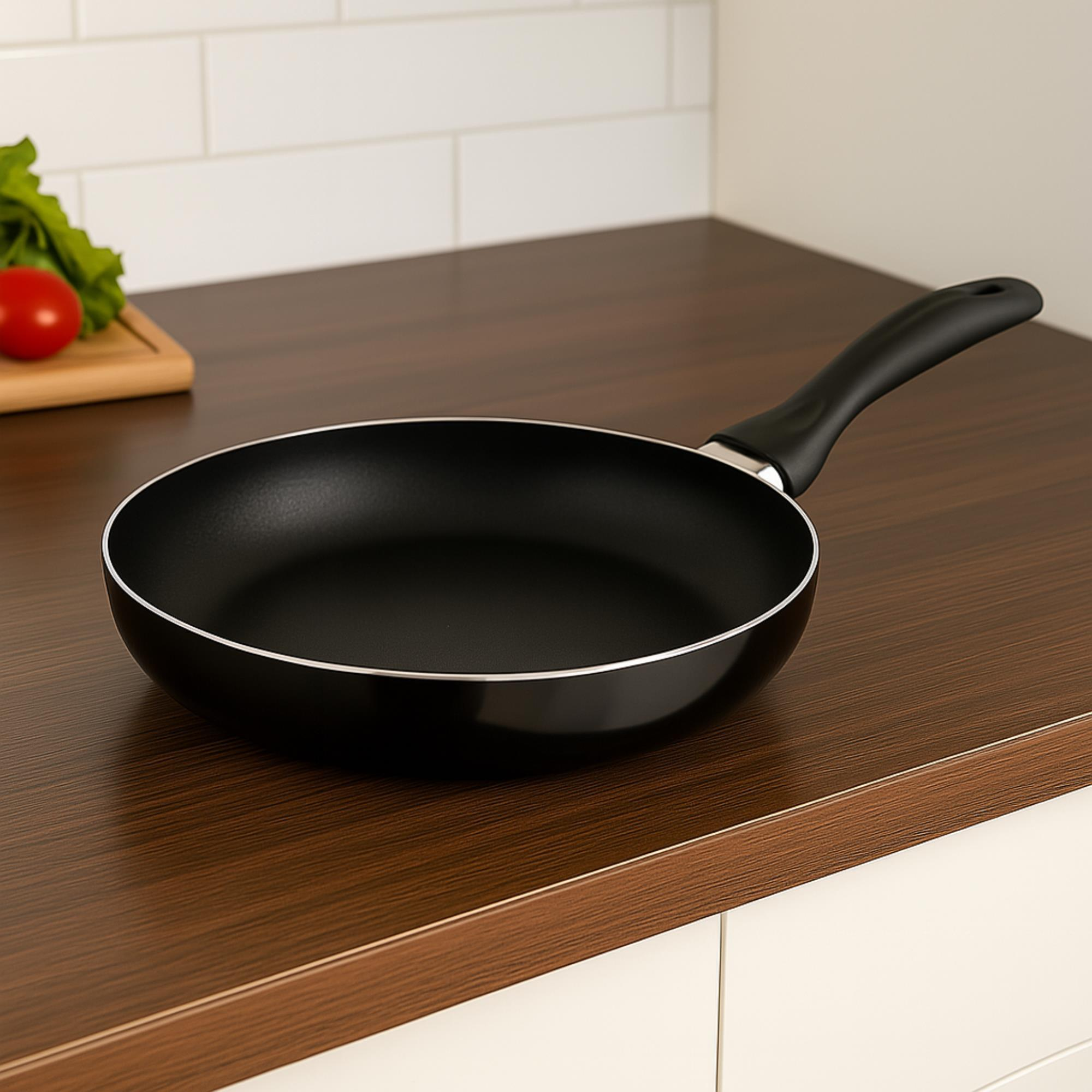 Sartén negro sobre encimera de madera. Tomate y lechuga sobre tabla en el fondo.