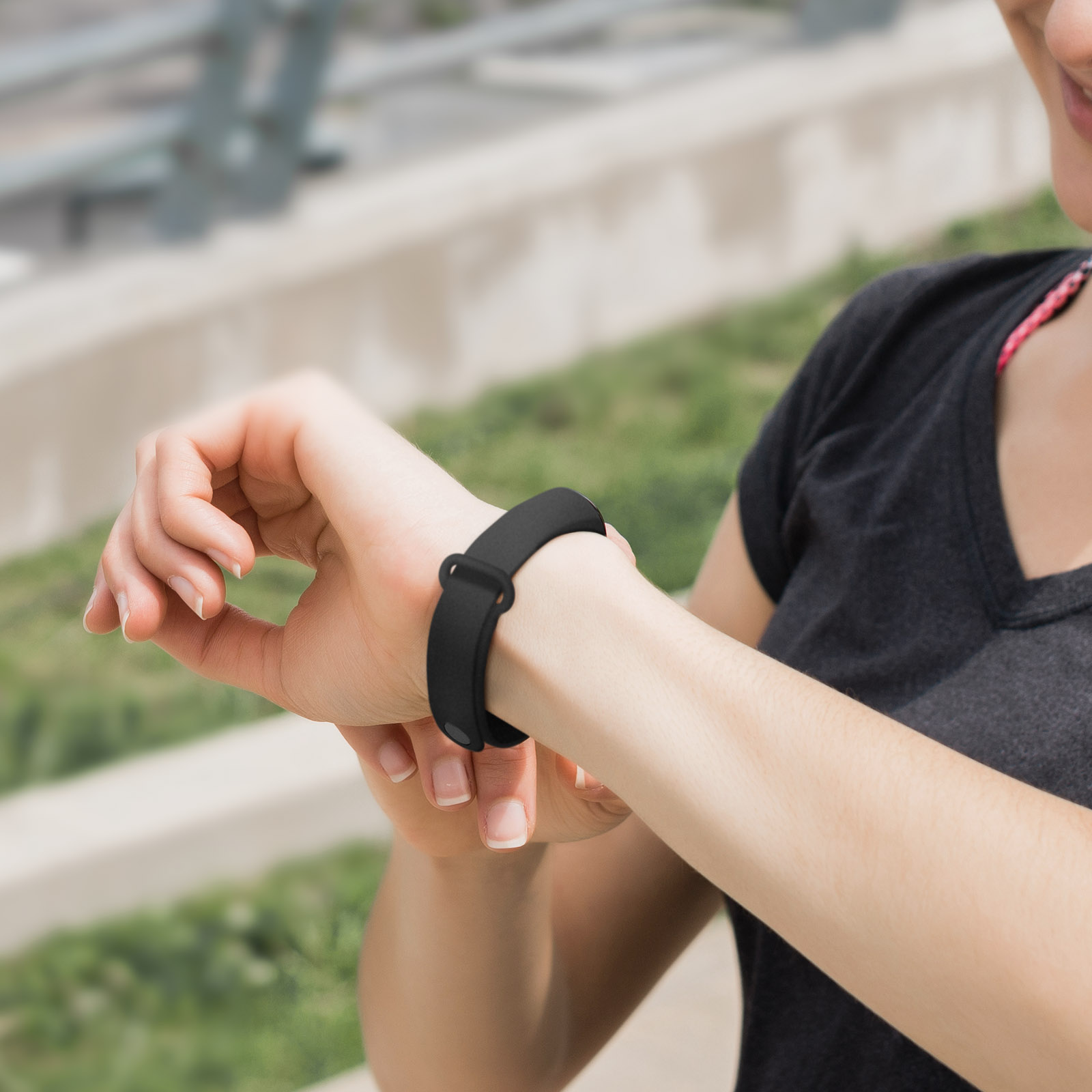 Una donna indossa un fitness tracker nero al polso. Sta guardando il tracker. Sfondo sfocato.