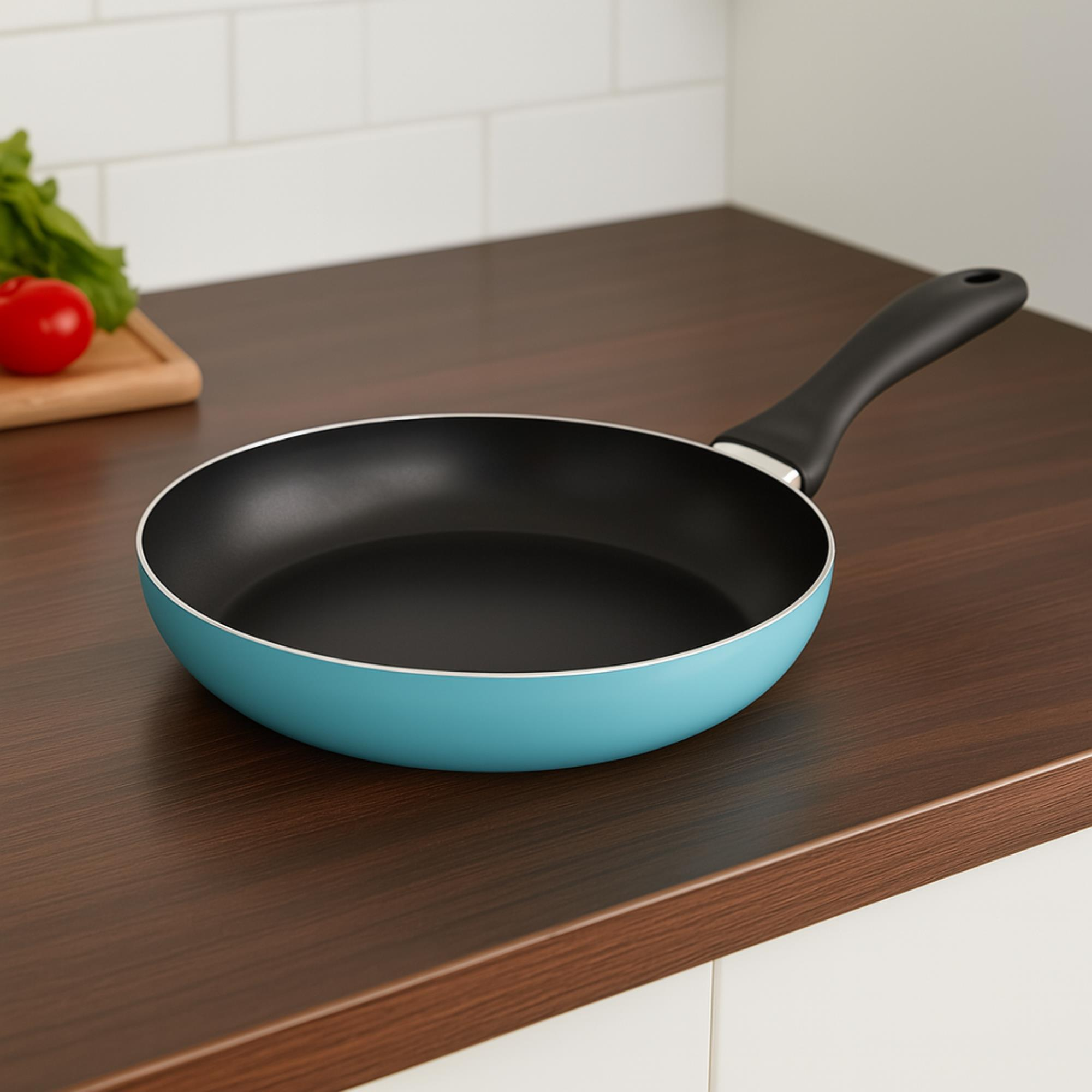 Una sartén turquesa sobre una encimera de madera oscura. Un tomate y verduras sobre una tabla de madera.