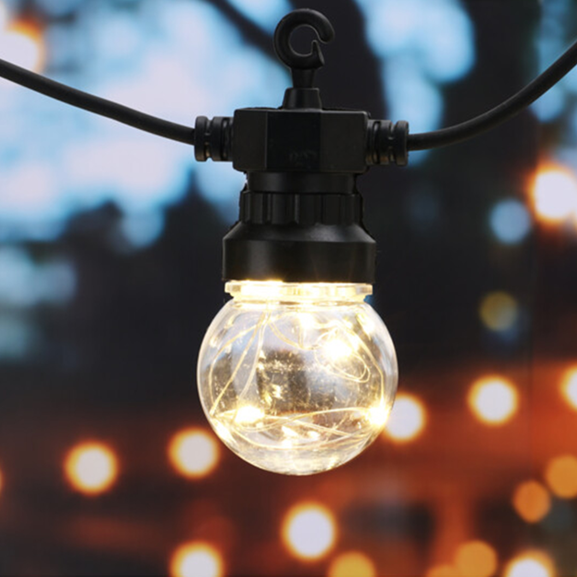 Una bombilla redonda y transparente con luces de hadas internas cuelga de un cable negro. El fondo está borroso con luces bokeh cálidas.