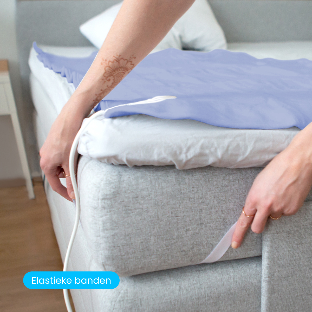 A person is putting a blue sheet on a bed. The sheet has elastic bands. The person has a henna tattoo on their arm.