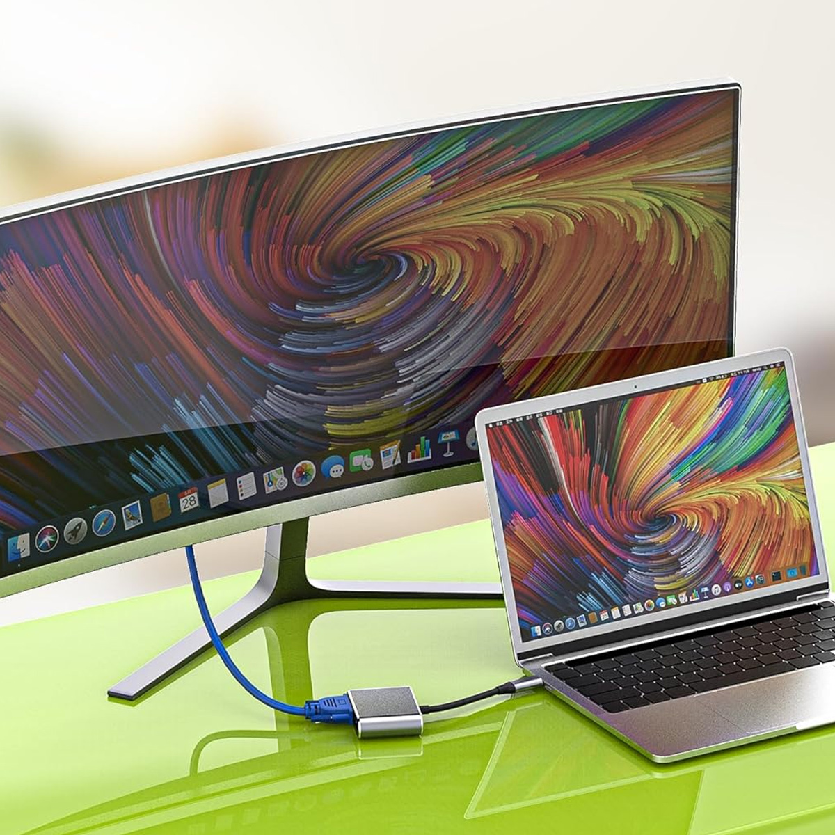 Ein Laptop und ein Monitor zeigen bunte Wirbelmuster. Ein blaues Kabel verbindet den Monitor mit einem silbernen Adapter.