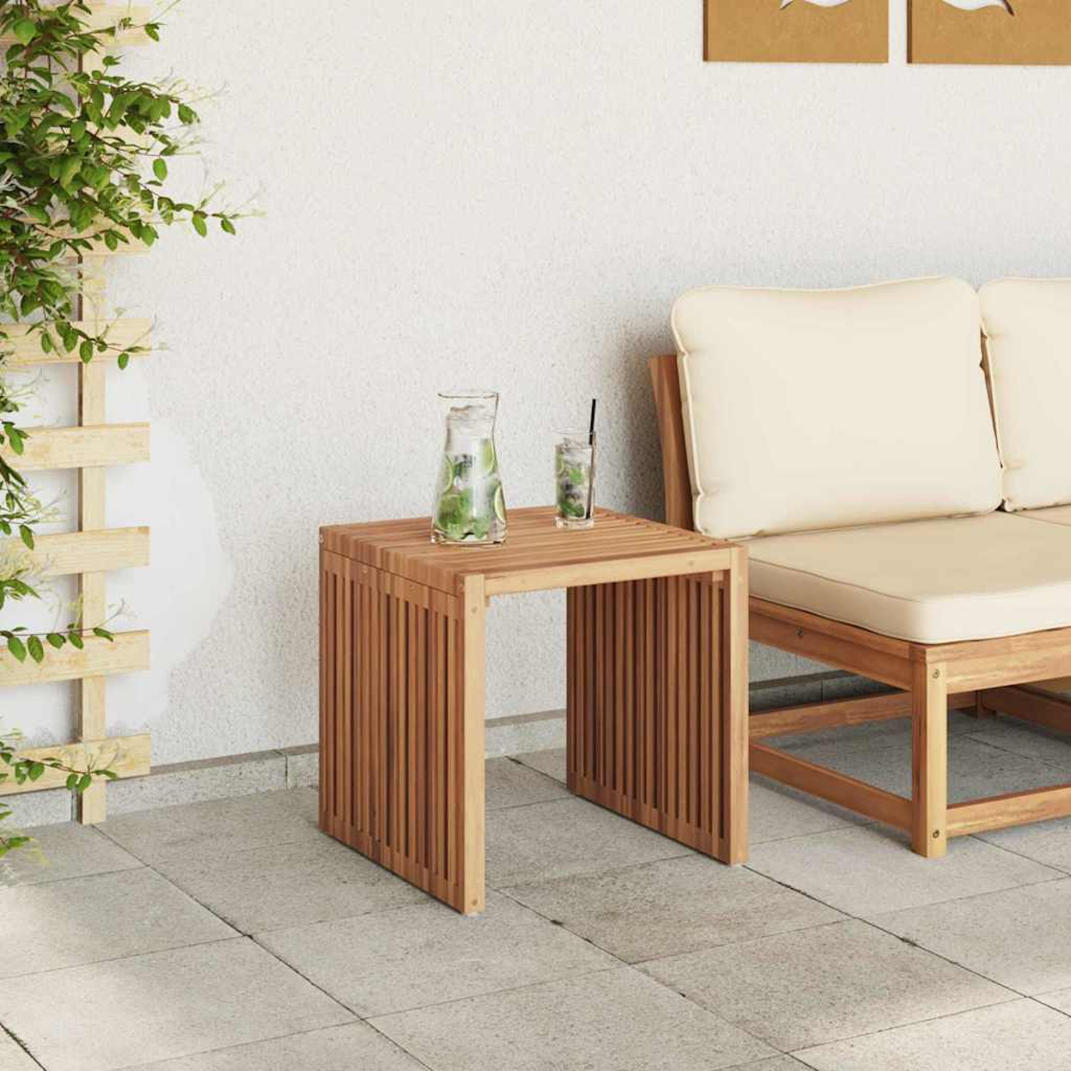 Ein Holztisch mit einem Krug und einem Glas mit Strohhalm. Rechts ist ein Sofa. Links sind grüne Pflanzen.