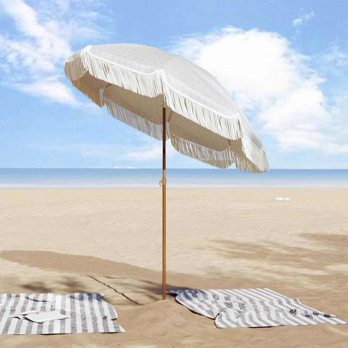 Un ombrellone da spiaggia bianco con frange sulla sabbia. Due coperte a righe e l'oceano sullo sfondo.