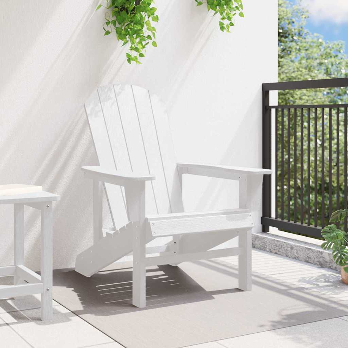 Una silla Adirondack blanca en un patio. Plantas verdes cuelgan desde arriba. Una pequeña mesa blanca está a la izquierda. Una barandilla negra está en el fondo.