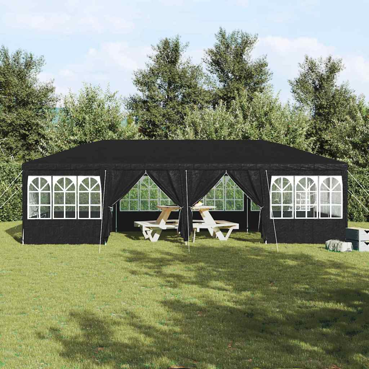 Ein schwarzer Pavillon mit weiß gerahmten Fenstern und zwei Picknicktischen im Inneren, auf Gras mit Bäumen im Hintergrund.